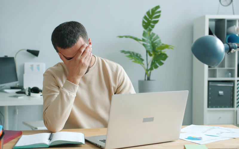 Mann reibt sich vor dem Laptop das Gesicht